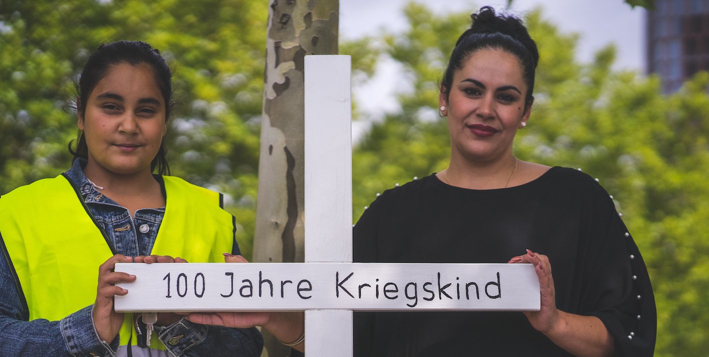 Zwei Menschen mit einem Kreuz des Erinnerungsprojekts 100 Jahre Kriegskind